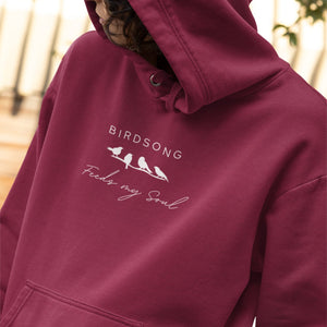 Maroon hoodie with the words Birdsong feeds my should above and below a white graphic of 4 birds on a branch. Worn by a woman.