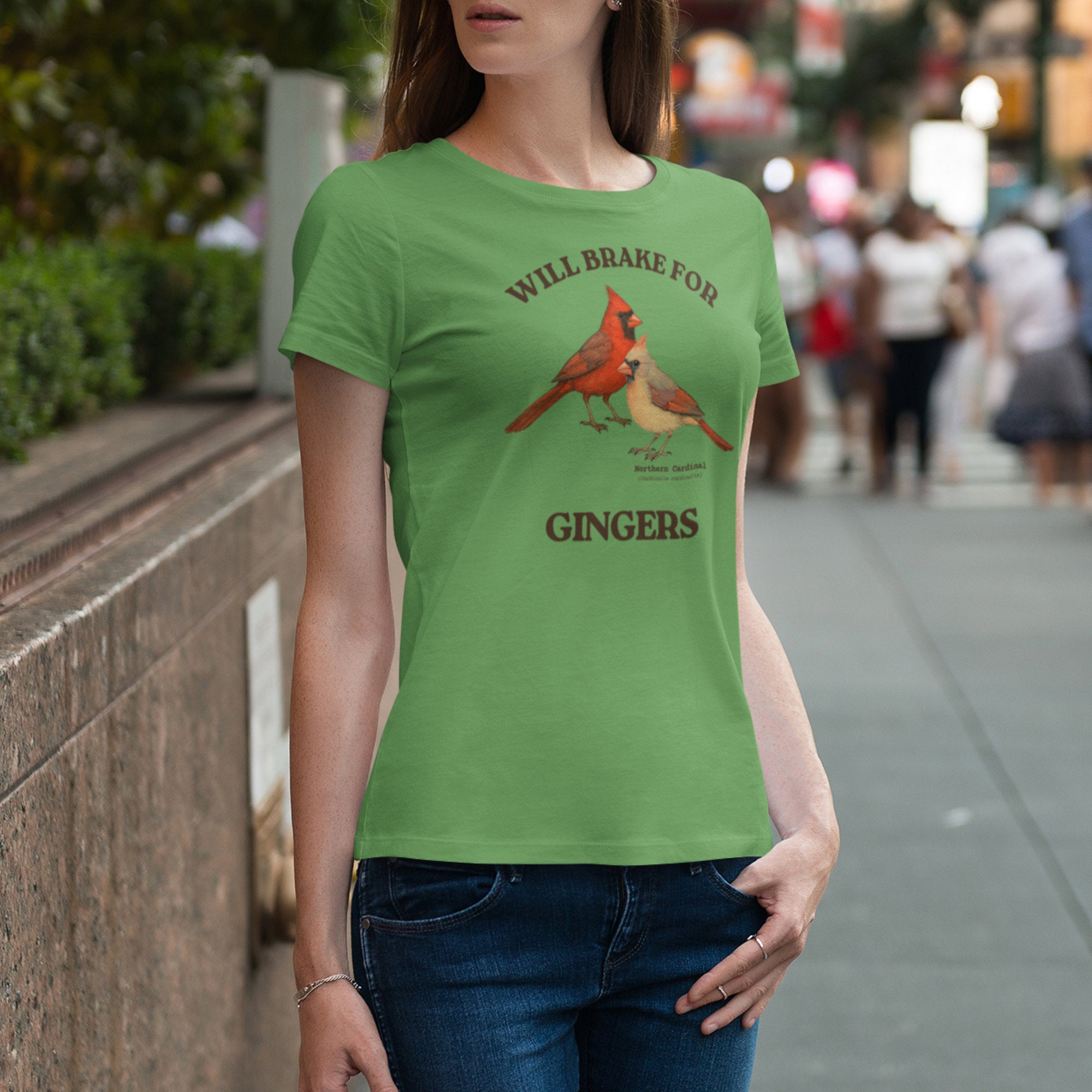 Person wearing a green t-shirt with cardinal design and text on a city street.