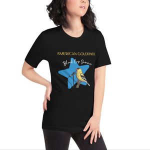 Black unisex bird shirt featuring an American goldfinch singing into a microphone with a list of dates and cities on the back where the bird is commonly seen. Worn by a woman.