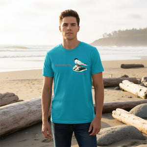 Aqua blue unisex crew neck t-shirt with a graphic of an Arctic Tern on a rock, and the words "Awaiting My" next to it in a fun pun. The words Arctic Tern and the scientific name of Sterna Paradisaea are below the bird. Worn by a man on the beach.