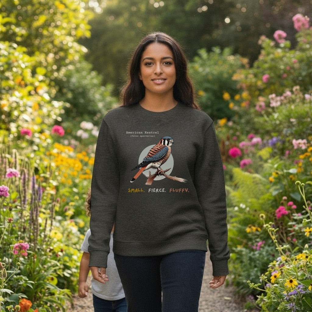 Dark heather grey unisex bird sweatshirt with the words, "Small. Fierce. Fluffy" below an illustration of an American Kestrel. Worn by a woman.