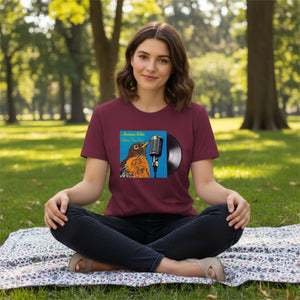 Woman sitting on a blanket in a park wearing a Concert style women's relaxed fit tee in maroon; featuring an American Robin. 