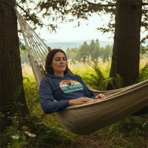 Heather navy long sleeved hoodie birding tee with a retro backyard birder design on the front. Worn by a woman relaxing on a hammock.
