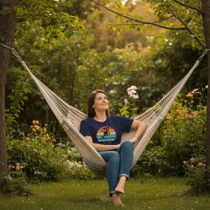 Navy blue women's bird shirt with a retro sun design outlining a bird feeder with the words Backyard Birder. Worn by a woman sitting in a garden setting in a hammock.
