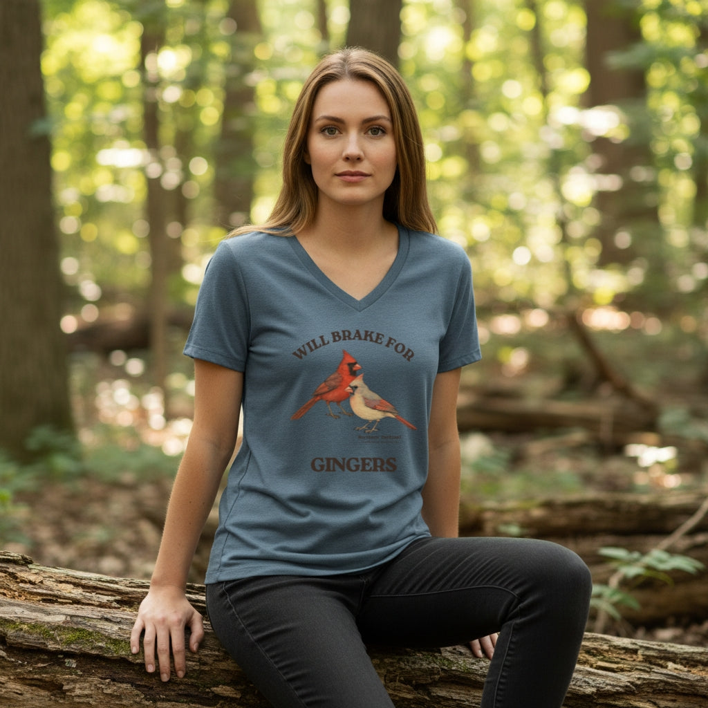 Woman wearing a heathered slate blue bird t-shirt with a graphic design of Northern Cardinals, sitting on a log.