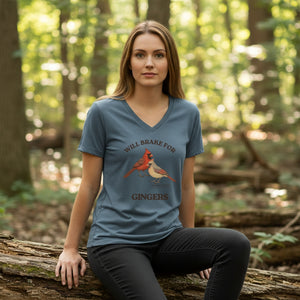 Woman wearing a heathered slate blue bird t-shirt with a graphic design of Northern Cardinals, sitting on a log.