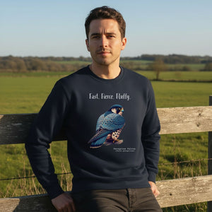 Navy crewneck bird sweatshirt with a peregrine falcon under the words, Fast, Fierce, Fluffy. Worn by a man leaning against a fence in a field.