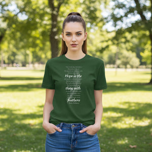 Woman wearing a green t-shirt with Emily Dickinson's Hope is the Thing with Feathers poem in white text, whilst in a park.