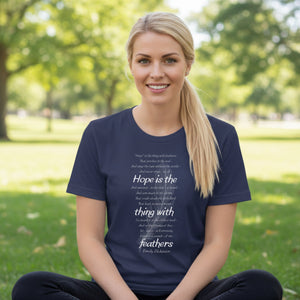 Woman wearing a navy blue t-shirt with Emily Dickinson's Hope is the Thing with Feathers poem in white text, whilst in a park.