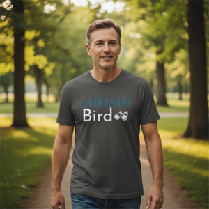 Grey bird shirt with the words, "Old Enough To Bird" and a pair of binoculars on the front. Worn by a man walking in a park.