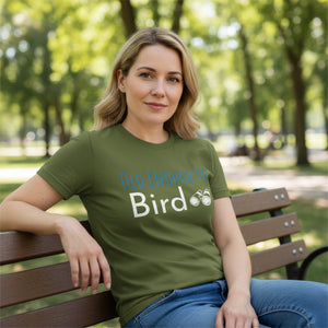 Olive green bird shirt with the words, "Old Enough To Bird" and a pair of binoculars on the front. Worn by a woman sitting on a park bench.