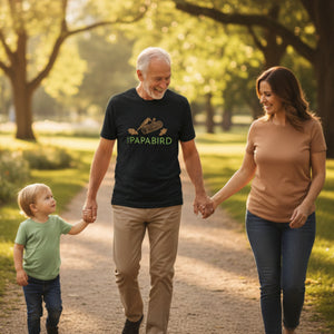 Grandfather, daugther and grandchild walking in a park, the man is wearing a charcoal black 'The PAPABIRD' t-shirt featuring a woodpecker on a log and oak leaves.