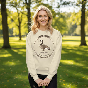 Unisex off-white bird sweatshirt with a canada goose on the front and a park department theme.  Worn by a woman in a park.