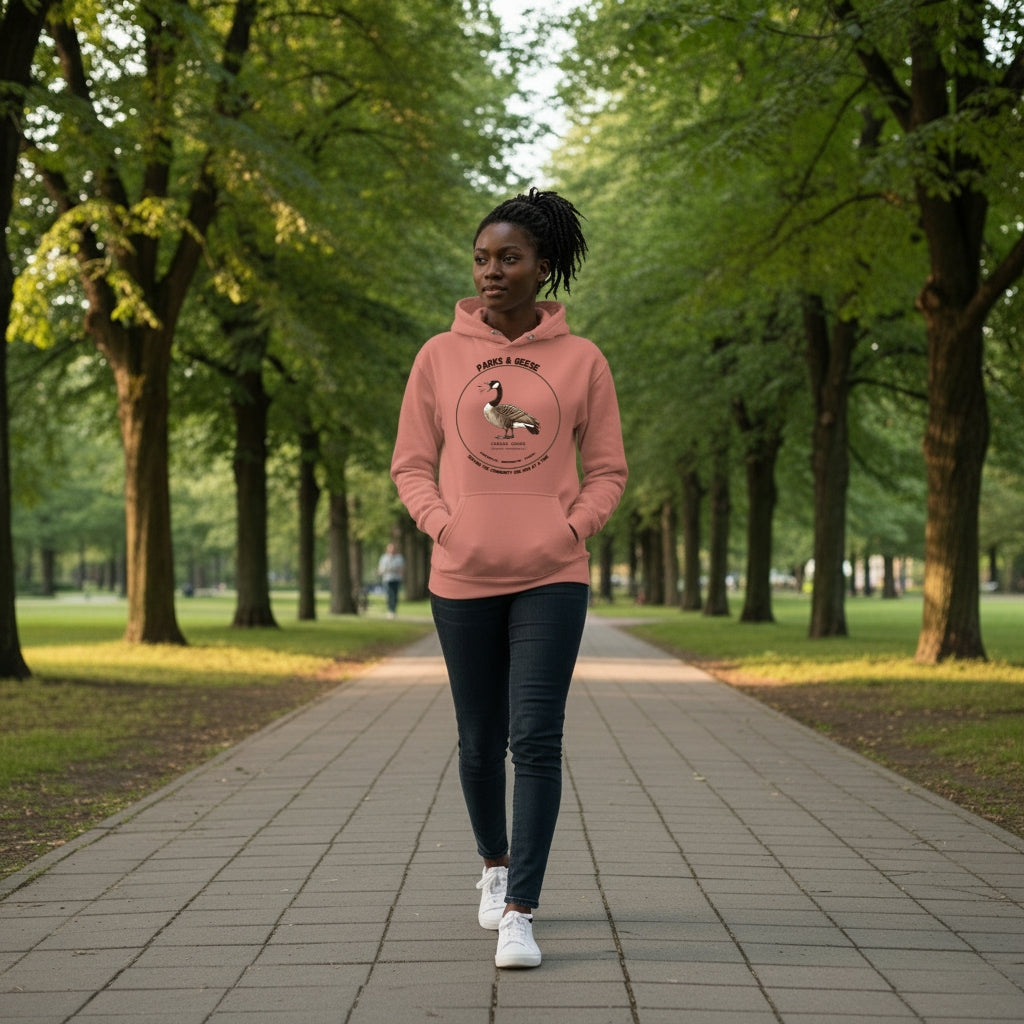 Unisex dusty rose bird hoodie with a canada goose on the front and a park department theme. Worn by a woman walking in a park.