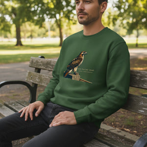 Green birding sweatshirt with an artistic depiction of a red-tailed hawk sitting on a fence and the common and scientific names for the bird next to it. Worn by a man sitting on a bench.