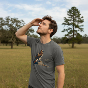 Gray bird shirt with an artistic depiction of a red-tailed hawk sitting on a fence and the common and scientific names for the bird next to it. Worn by a man standing in a field.