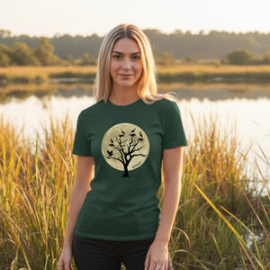 Green unisex bird shirt with a full moon outlining a heron rookery.  Worn by a woman by a wetland at sunset.