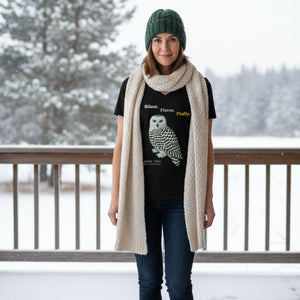 Person wearing a black t-shirt with a snowy owl design, green beanie, and beige scarf in a snowy outdoor setting.