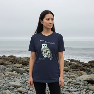 Person wearing a navy blue t-shirt with a snowy owl design on a rocky beach.