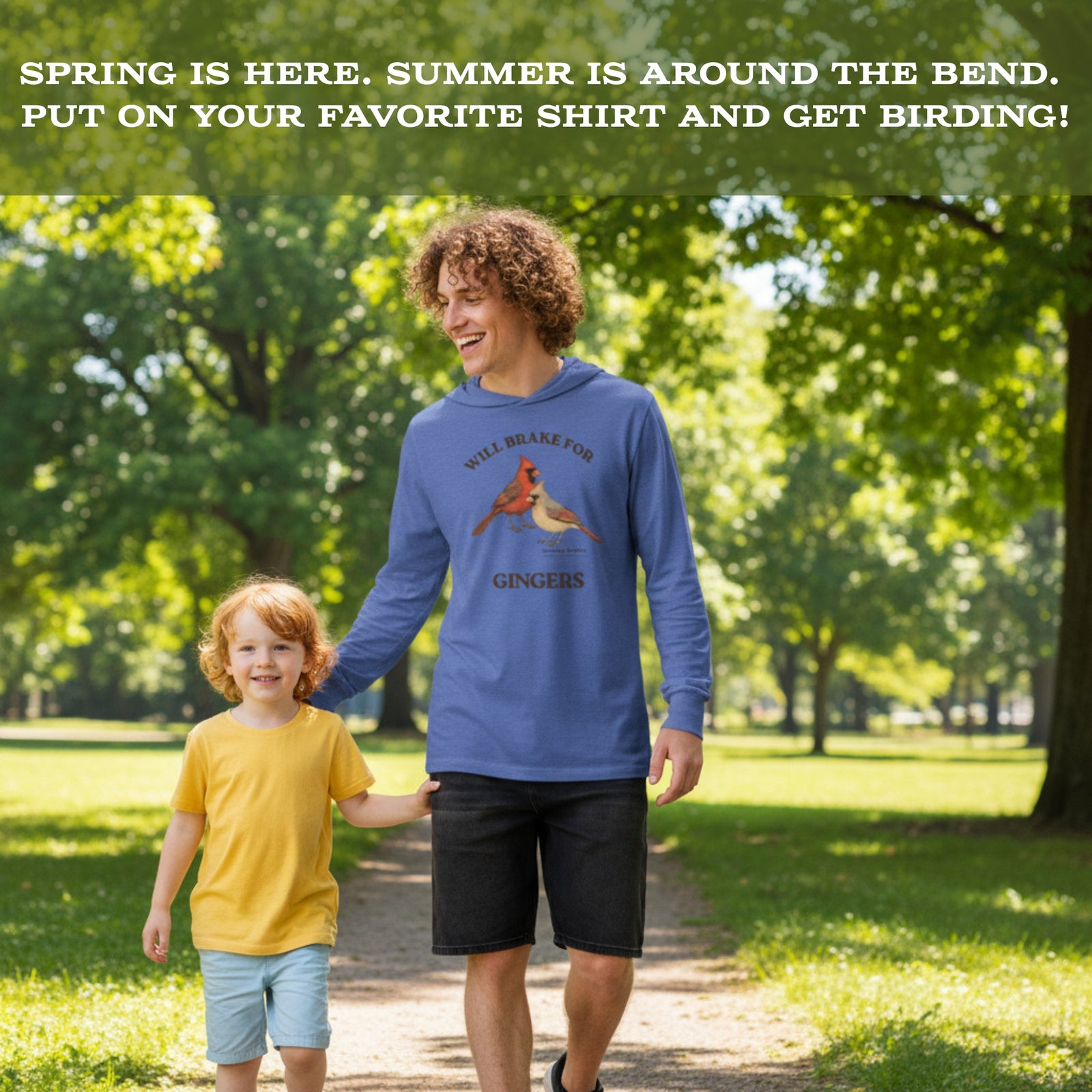 Man walking in a park with his child. The man is wearing a long-sleeved hooded tee with a northern cardinal design.