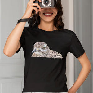 Black unisex bird shirt with a lifelike illustration of a Spotted Thickknee on the front and the words Spotted Thickknee in small print below, with the scientific name included. Worn by a woman taking a picture.
