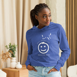 Heather royal blue long sleeved and hooded tee with fun, "Easily Distracted, Mostly by Birds" saying on the front, with a smiley face looking up at a flock of birds. Worn by a woman in a home.
