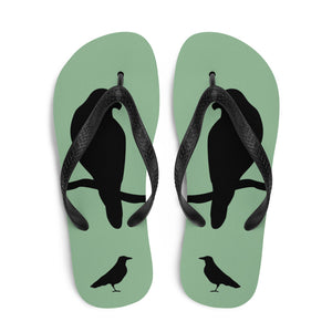A pair of sea green flip-flops with black strap and a silhouette of a crow on a branch.